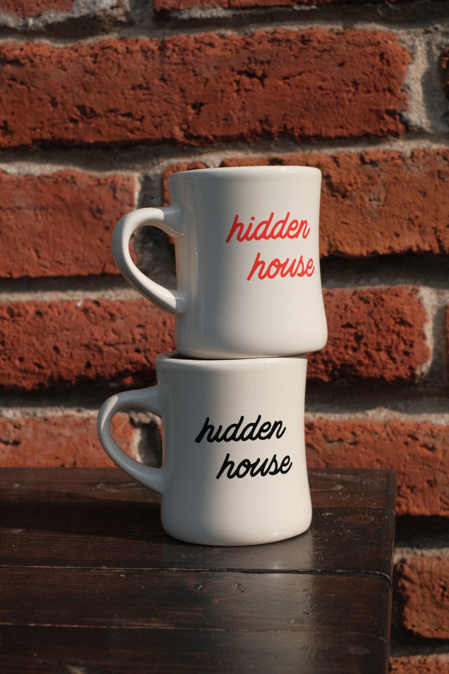 Inverse text of cursive "hidden house" logo shown on diner mugs.