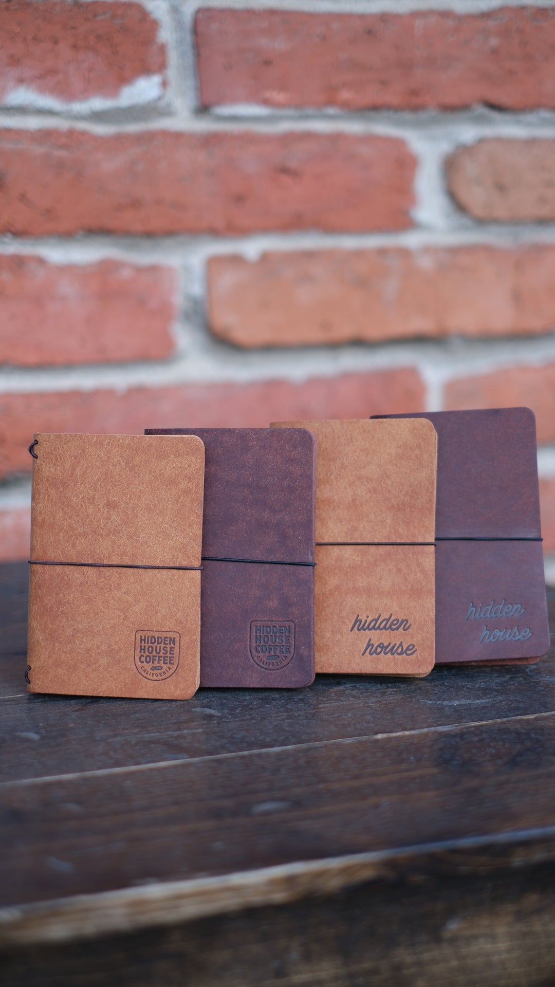 Picture of four leather journals stacked, with variation of colors and two different Hidden House Coffee logos.