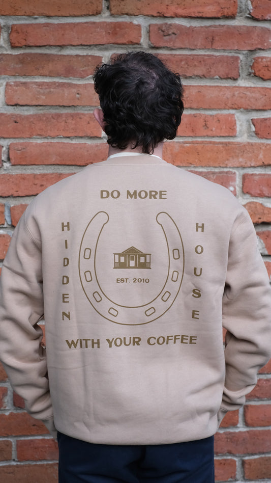 Model showing Back of crew neck sweatshirt featuring HHC artwork that says "Do more with your coffee, hidden house, established 2010".