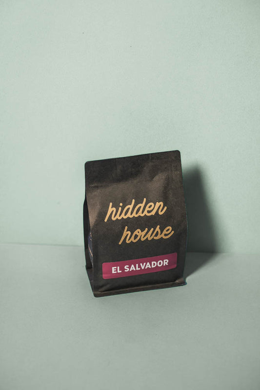 A picture of a black coffee bag with a dark purple label that says El Salvador
