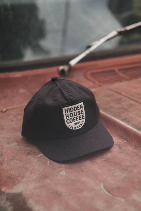 Image of black hat that has hidden house coffee embroidered on it.