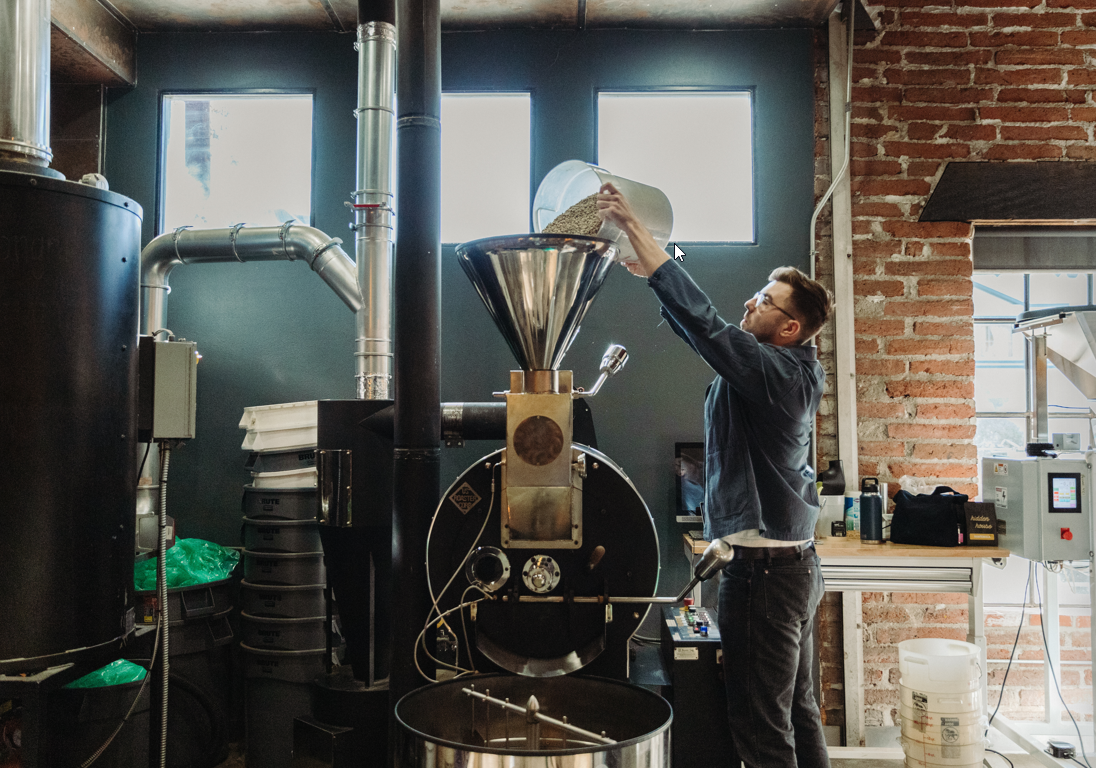 Image of man loading green coffee beans into a coffee roaster.