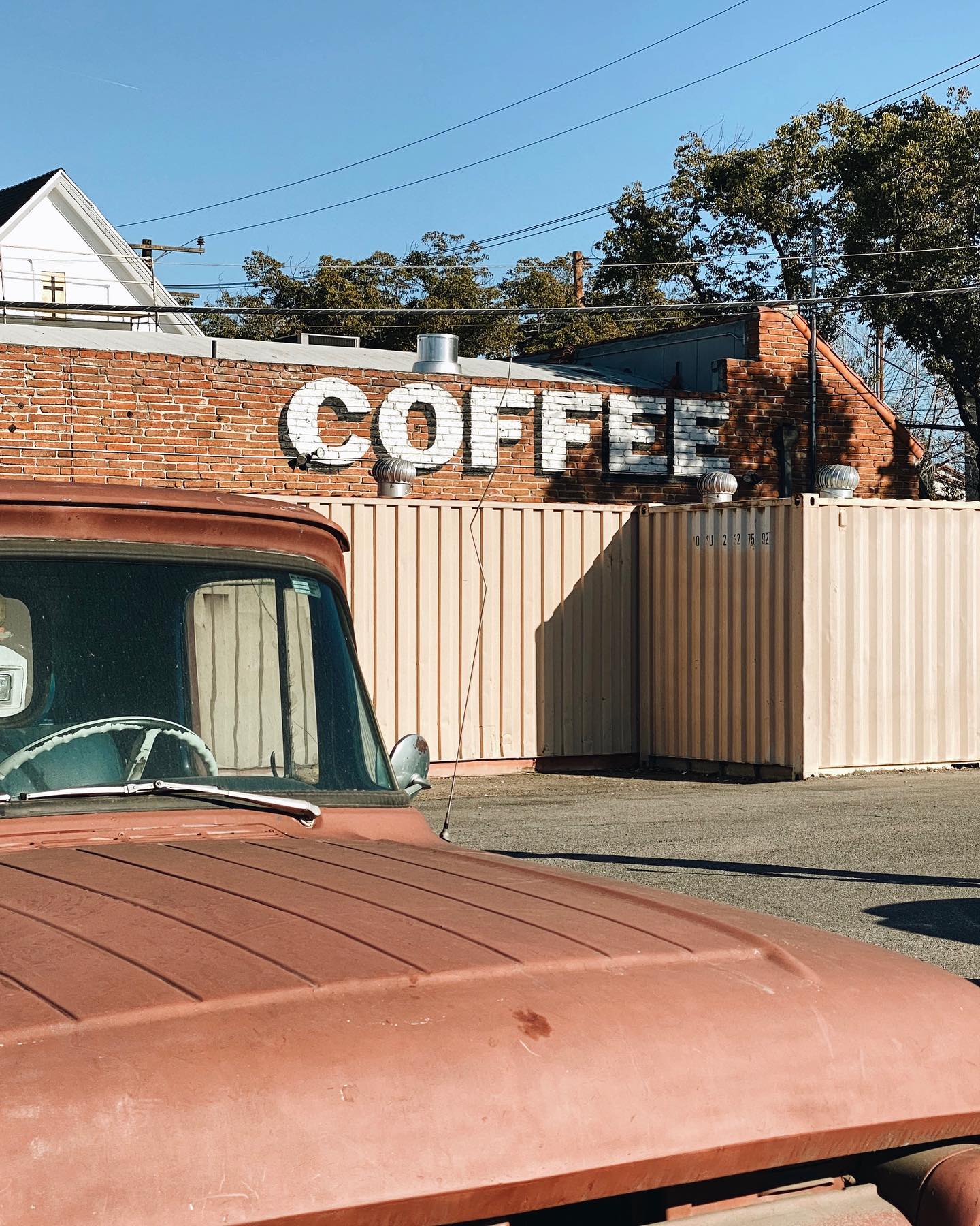 Image of a red truck, with Hidden House Coffee Santa Ana in the rear. "Coffee" is spelled out with white paint on the wall.