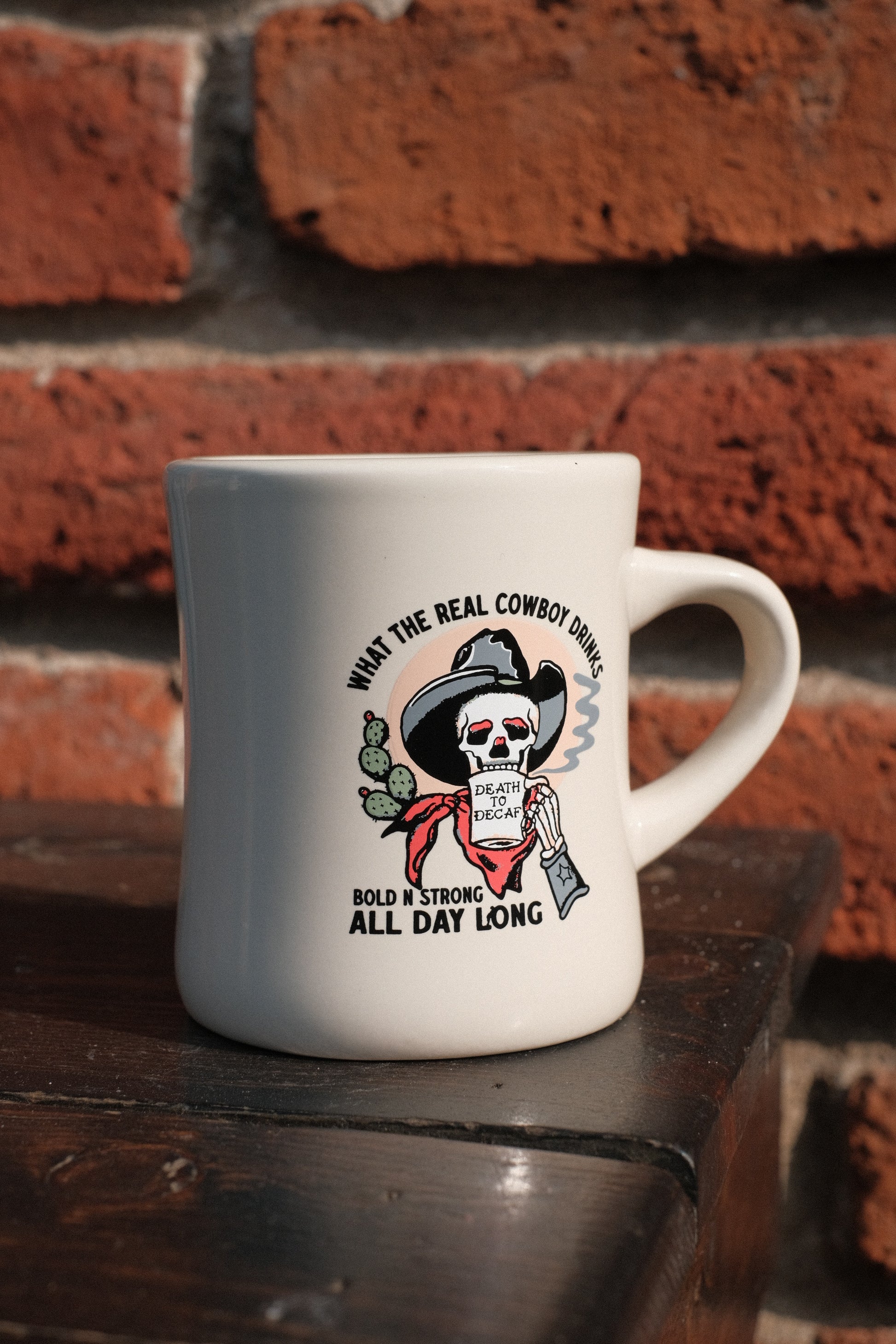 El Ray design shown on diner mug, "What the real cowboy drinks, bold n strong all day long" with cowboy drinking out of "death to decaf" mug. 