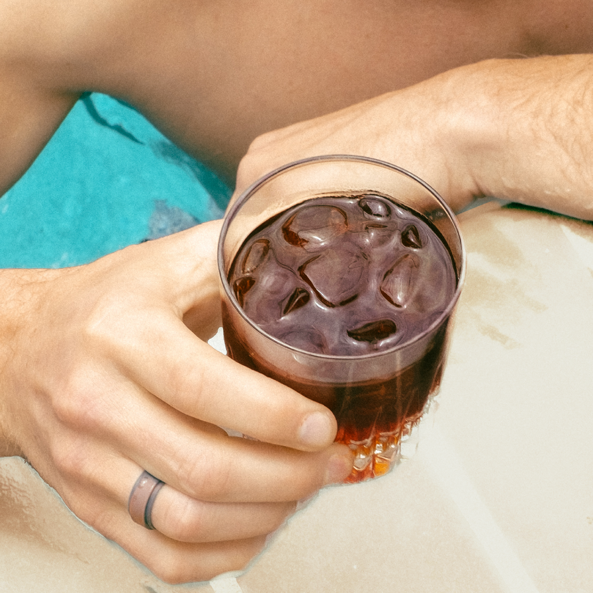 Photo of man holding clear glass off iced coffee at the side of a pool